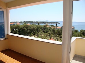 A balcony with a view of a coastal landscape, including trees, buildings, and a body of water. - One Bedroom Apartment with Balcony and Sea View (Petrcane)