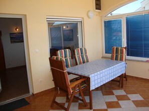A dining area with a table and chairs, a window with blinds, and a door leading to another room. - One Bedroom Apartment with Balcony and Sea View (Petrcane)