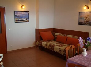 A room with a sofa, a table with a vase of flowers, and two wall-mounted lamps. - One Bedroom Apartment with Balcony and Sea View (Petrcane)