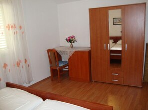 Quarto com guarda-roupa de madeira, cama, escrivaninha com cadeira e janela com cortinas.