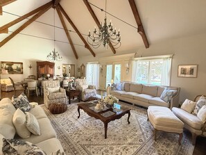 A spacious living room with a high ceiling, a chandelier, a sofa set, a coffee table, and a dining area with chairs and a table. - Lovely 4-bedroom house with AC in pleasant Tulsa neighborhood (Tulsa)