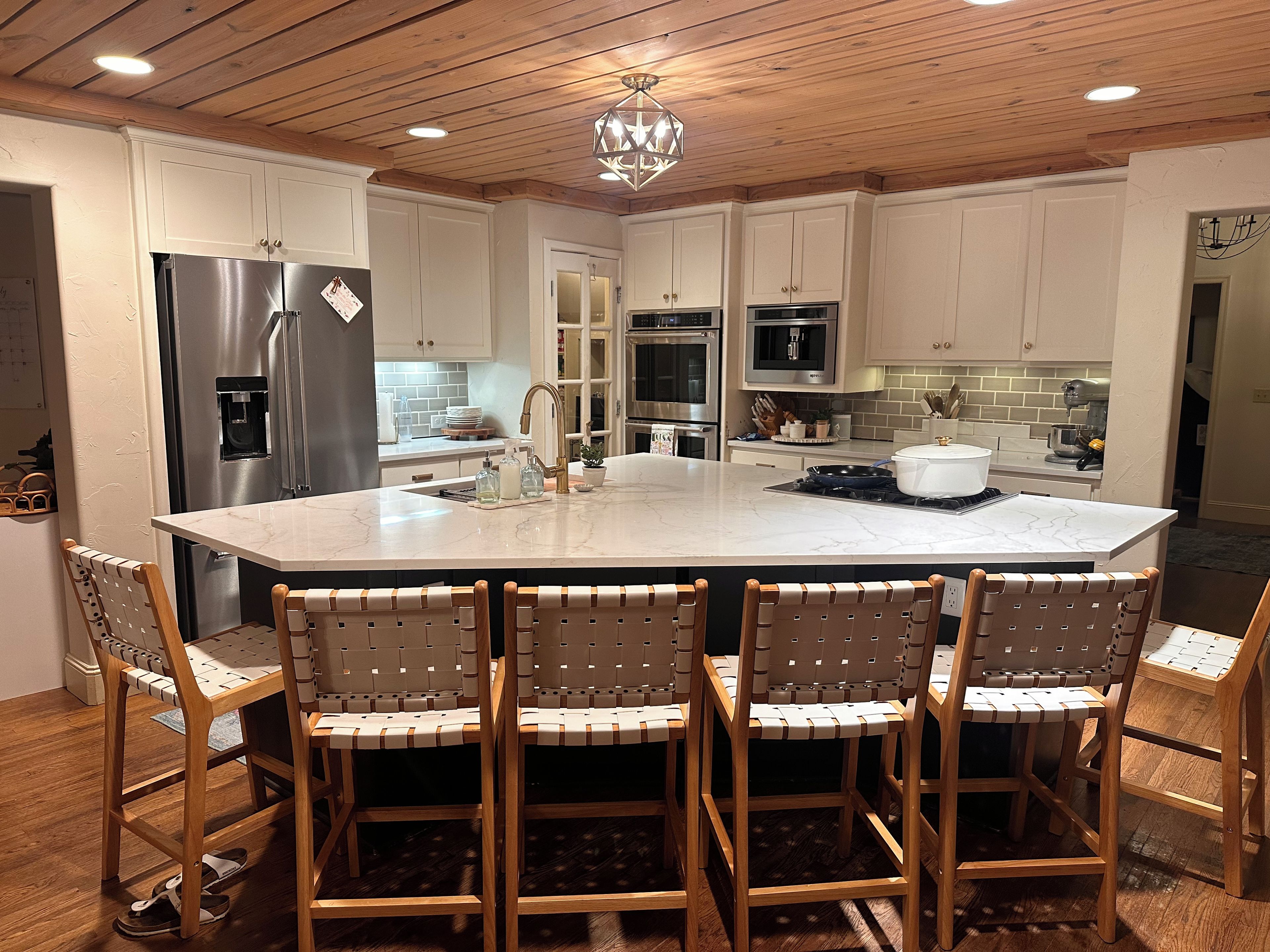 A kitchen with a large island, white cabinets, stainless steel appliances, and wooden chairs.