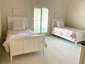 Ein Schlafzimmer mit zwei Betten, einem Fenster mit Jalousien und Wanddekorationen.