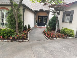 A residential property with a paved driveway leading to a front door, surrounded by landscaped gardens and mature trees. - Lovely 4-bedroom house with AC in pleasant Tulsa neighborhood (Tulsa)
