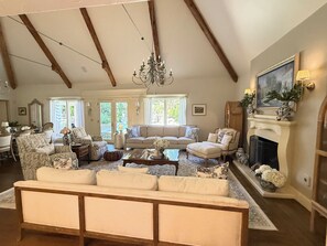 A spacious living room with a fireplace, a chandelier, and a large window providing natural light. - Lovely 4-bedroom house with AC in pleasant Tulsa neighborhood (Tulsa)