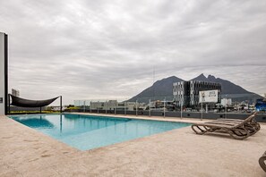 A swimming pool with a view of a mountain and modern buildings in the background. - ¡A pasos de Fundidora! Parking, Pool & Gym 6ppl (Monterrey)