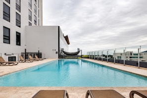 A rooftop pool with lounge chairs, a hammock, and a modern building in the background. - ¡A pasos de Fundidora! Parking, Pool & Gym 6ppl (Monterrey)