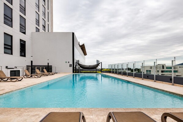 Ein Pool auf dem Dach mit Liegestühlen, einer Hängematte und einem modernen Gebäude im Hintergrund.