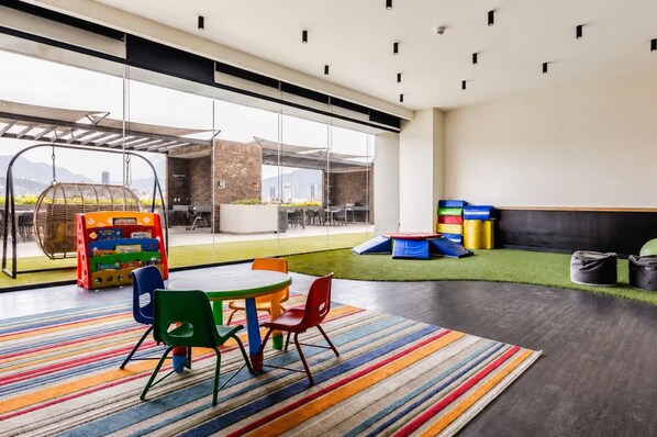 Un'area giochi indoor moderna con un tappeto colorato a righe, un'altalena sospesa e diverse strutture ludiche.