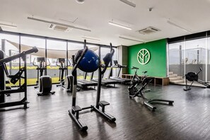 A gym with various exercise equipment, large windows, and a green wall with a logo. - ¡A pasos de Fundidora! Parking, Pool & Gym 6ppl (Monterrey)