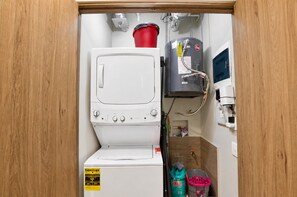 A compact bathroom with a white washing machine, a red bucket, a water heater, and a small shelf with toiletries. - ¡A Pasos de Fundidora! Gym, Pool, Parking 2B2b 8H (Monterrey)