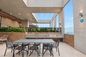 Een buiten eetgedeelte met een tafel en stoelen, uitzicht op de stad en een balkon met een hekwerk.