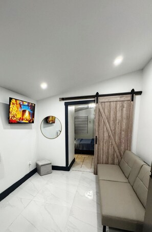 A modern living room with a sofa, a television, a mirror, and a sliding door leading to another room. - Private studio by Miami International Airport (Miami)