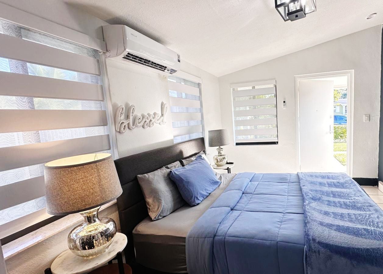 Un dormitorio con cama, lámpara de noche y aire acondicionado instalado en la pared.