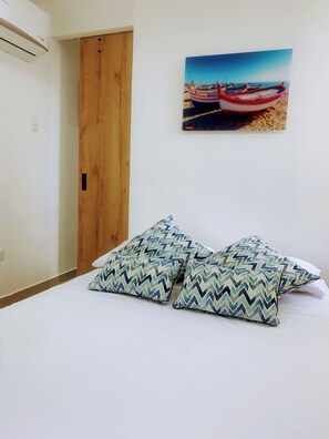 A bedroom with a bed, two patterned pillows, a wooden door, and a beach scene painting on the wall. - 8b4 en El Laguito: cerca del mar, piscina y wifi (Cartagena de Indias)