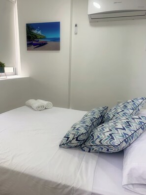 Ein Hotelzimmer mit Bett, einem Strandbild, einem Fenster mit Pflanze und einer Klimaanlage.