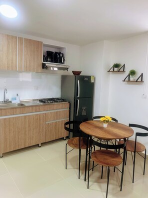 A compact kitchen with a gas stove, a refrigerator, wooden cabinets, and a dining area with a table and chairs. - 8b4 en El Laguito: cerca del mar, piscina y wifi (Cartagena de Indias)