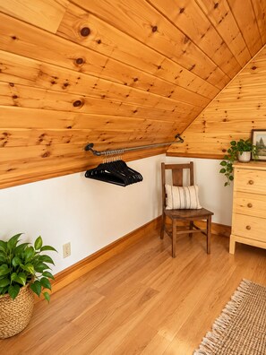 Ein Zimmer mit Holzboden, ein Holzbstuhl mit Kissen, ein Holzschrank und eine Kleiderstange.