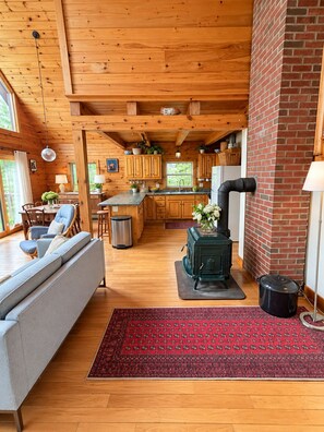 Ein gemütliches Blockhaus-Interieur mit Holzbalkendecke, einer Küchenzeile, einem Essbereich und einem Wohnbereich mit Sofa und Sesseln.