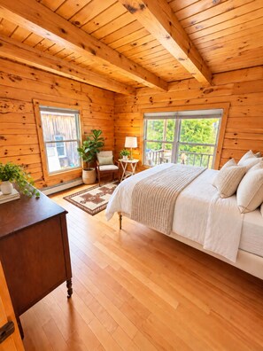 Ein Schlafzimmer einer Holzhütte mit einem Bett, einem Sessel, einem Tisch und einem Fenster.