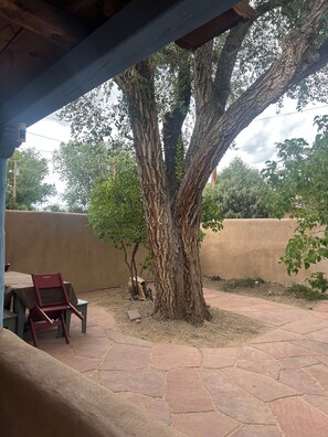 A covered outdoor area with a large tree, patio furniture, and a paved walkway. - Lovely 2-bedroom house in tranquil Taos. (Taos)