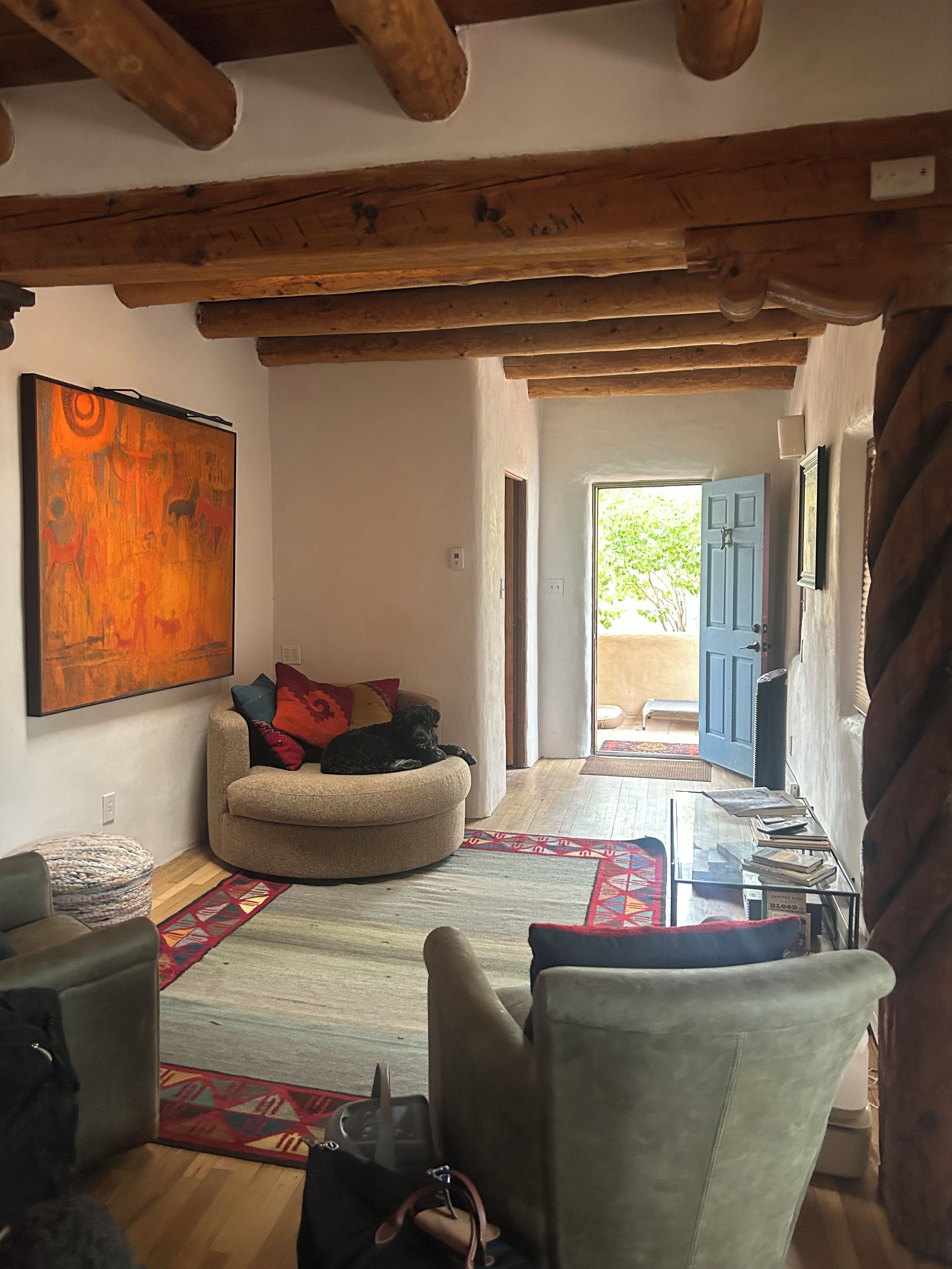 A living room with a sofa, a dog, a painting, and a view through an open door.