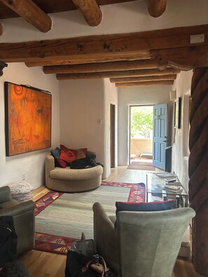 A living room with a sofa, a dog, a painting, and a view through an open door. - Lovely 2-bedroom house in tranquil Taos. (Taos)