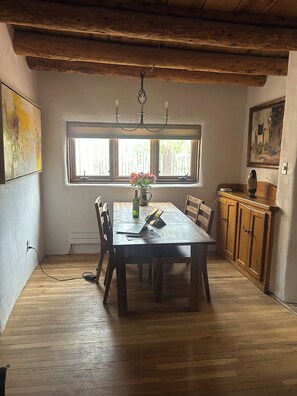 A dining area with a wooden table, chairs, a chandelier, and a window with a view. - Lovely 2-bedroom house in tranquil Taos. (Taos)