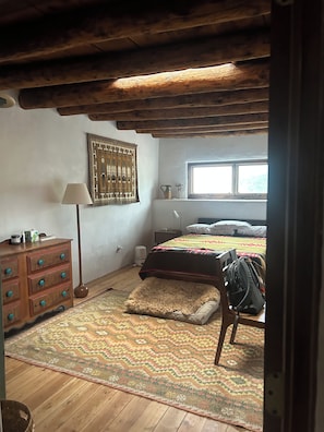 Ein Schlafzimmer mit Holzboden, einem Bett mit gemustertem Bettbezug, einem Nachttisch mit Lampe und einer Kommode mit Schubladen.