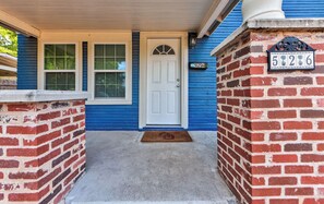 A house with a white door, blue siding, and a brick wall with a mailbox. - Charming 6BR Norman Home Perfectly Near OU and Campus Corner (Norman)