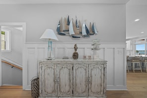 Un interior blanco con un aparador de madera desgastada, una lámpara y decoración de temática náutica.