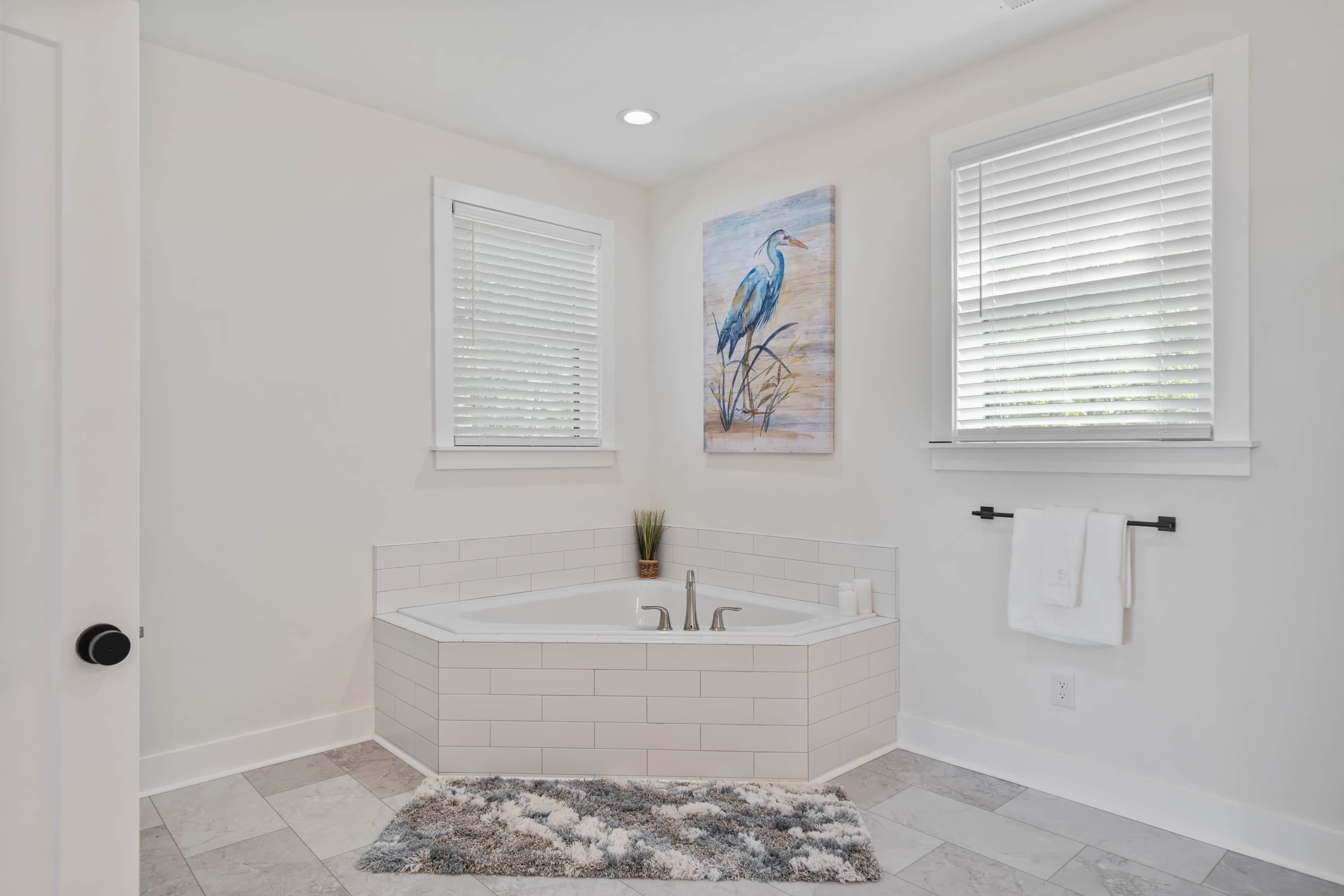 Un baño con una bañera blanca, un perchero para toallas y un cuadro de un pájaro.