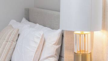 A neatly made bed with white linens and a single striped pillow, a bedside table with a lamp, and a painting on the wall.