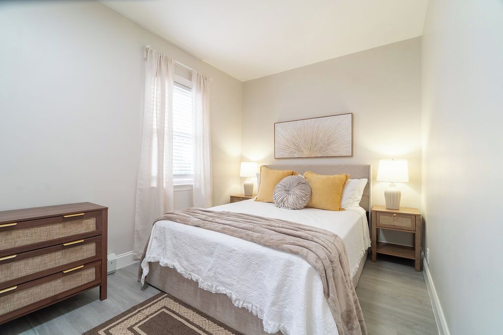 A bedroom with a bed, bedside tables, a dresser, and a window with curtains.