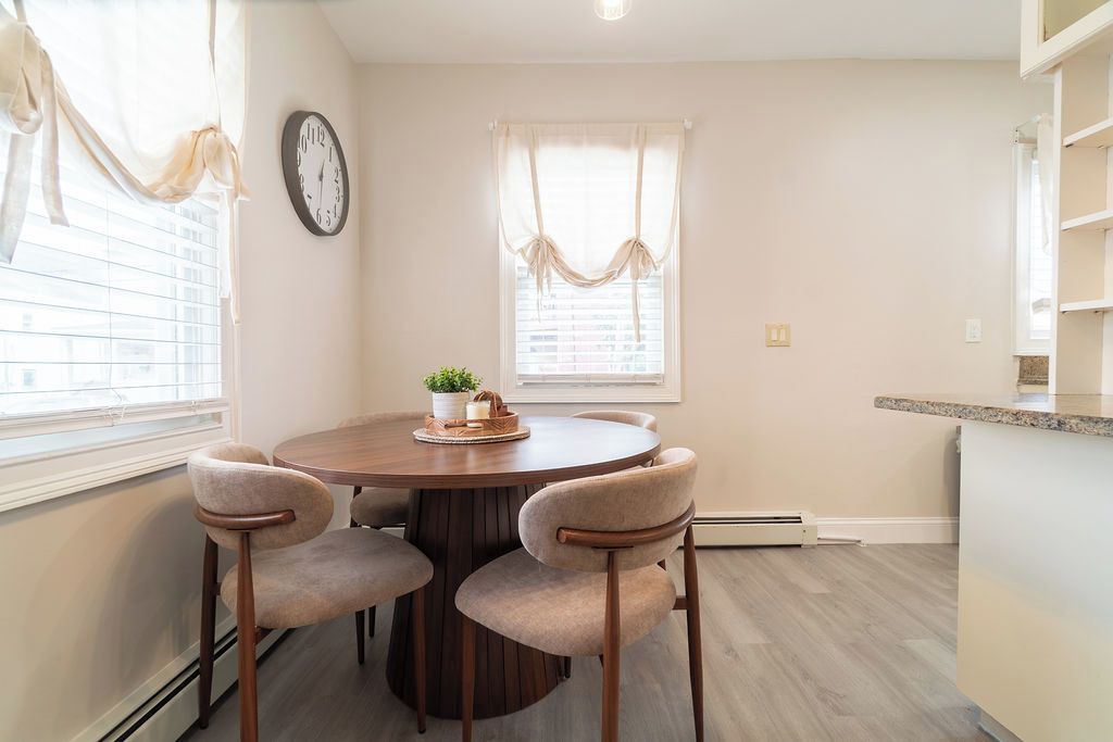 A dining area with a round table, four chairs, a clock, and a window with curtains.