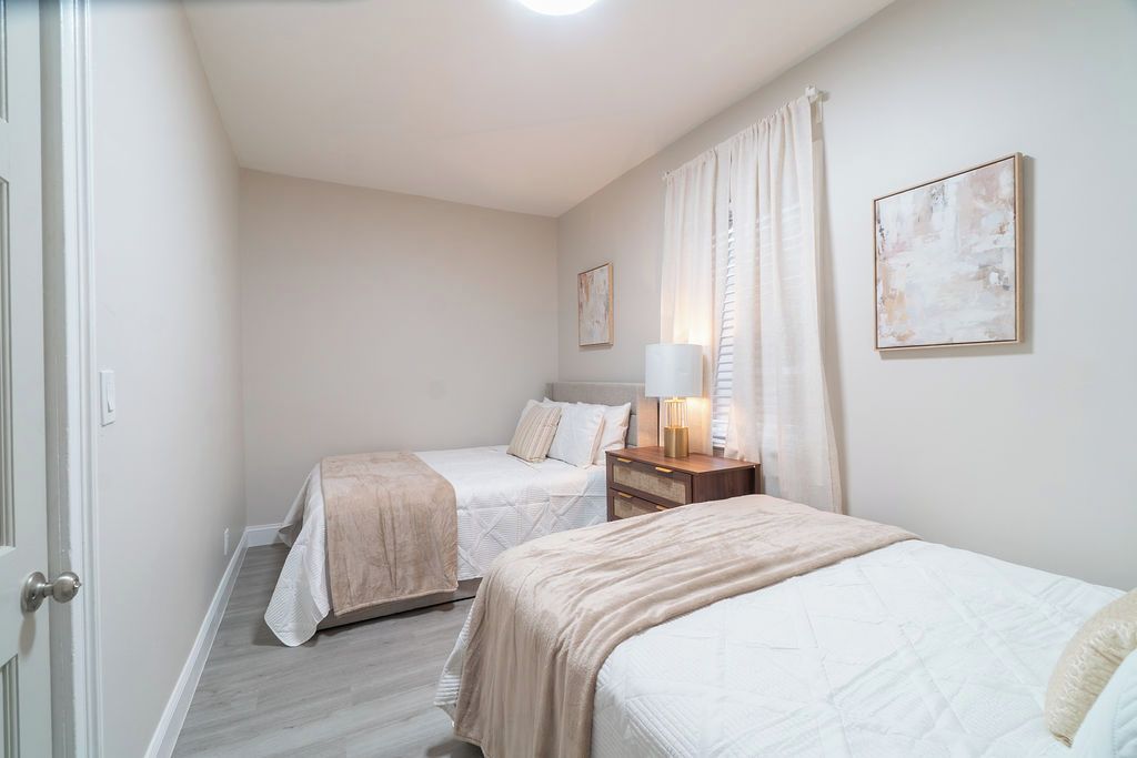 Ein Schlafzimmer mit zwei Betten, einem Nachttisch mit Lampe und einem Fenster mit Vorhängen.