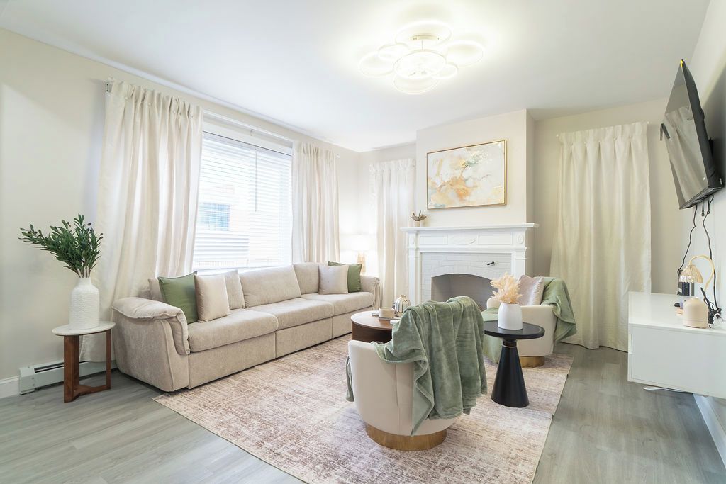 Ein Wohnzimmer mit einem beigen Sofa, einem runden Couchtisch, einem Kamin und einem an der Wand montierten Fernseher.