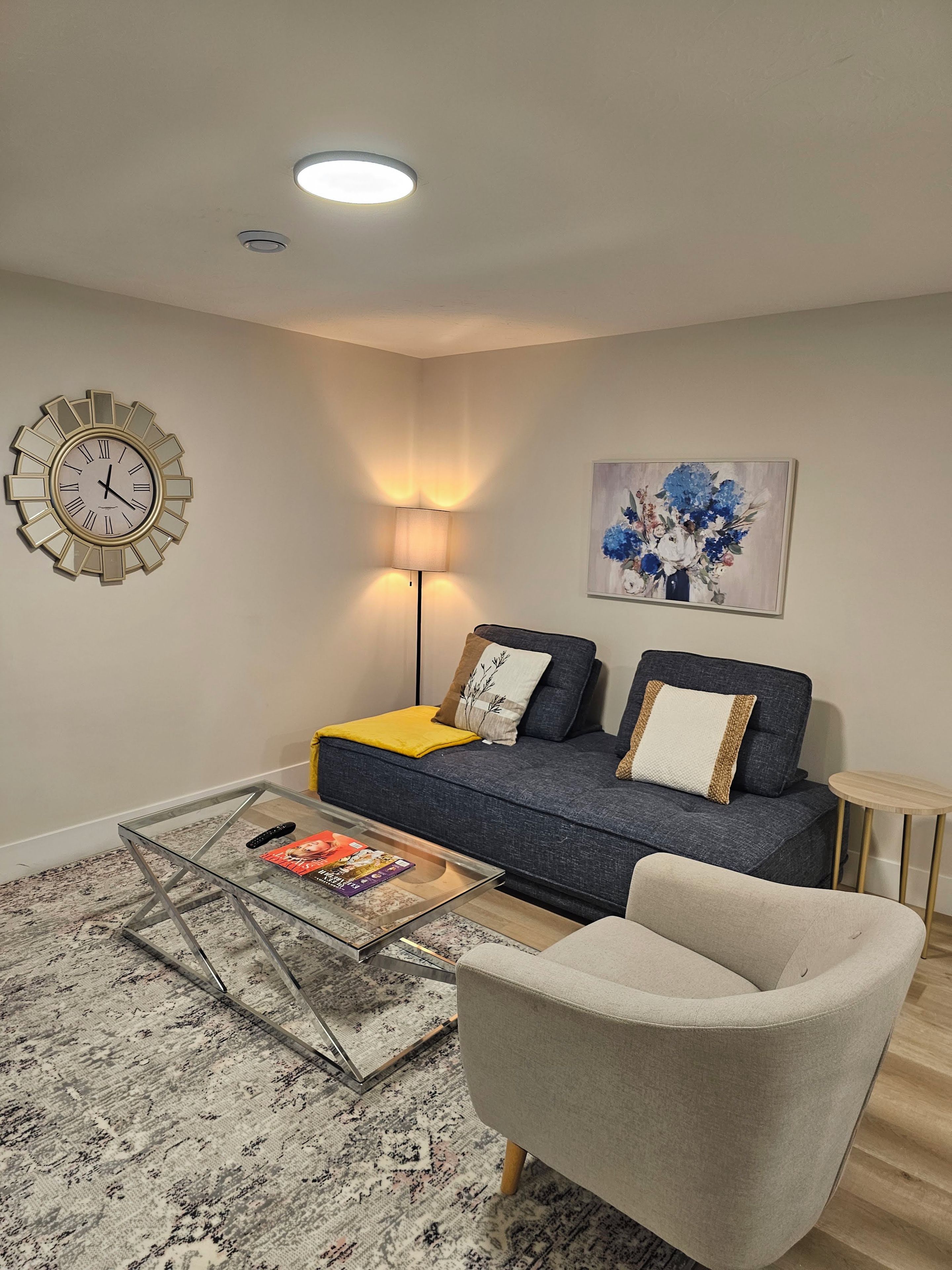 A modern living room with a sofa, armchair, coffee table, and a wall clock.
