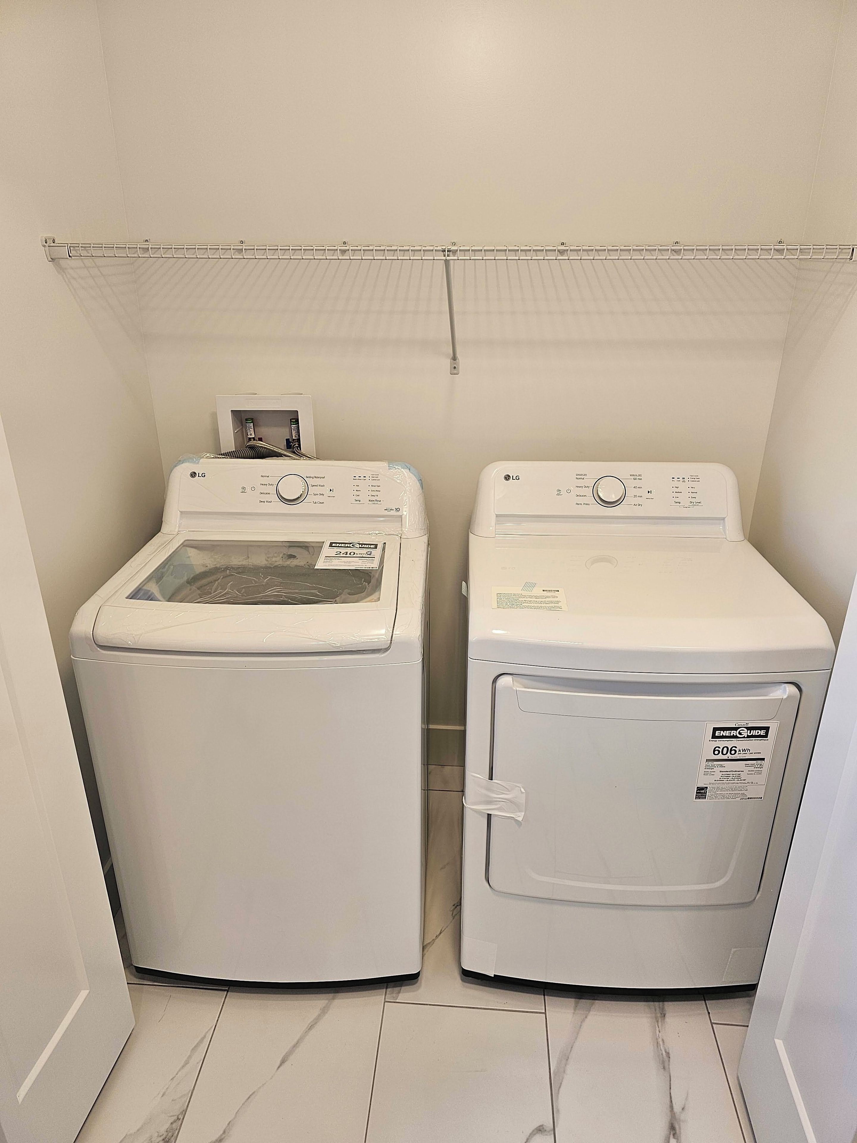 A laundry room with two white front-loading washing machines and a metal drying rack above.