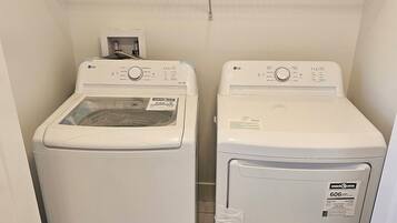 A laundry room with two white front-loading washing machines and a metal drying rack above.