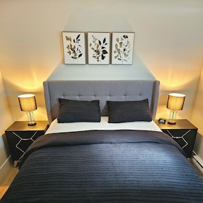 A bedroom with a bed, two nightstands, two lamps, and three wall-mounted floral artwork pieces. - Chester Luxury Suites - Brand New Moncton Getaway (Moncton)