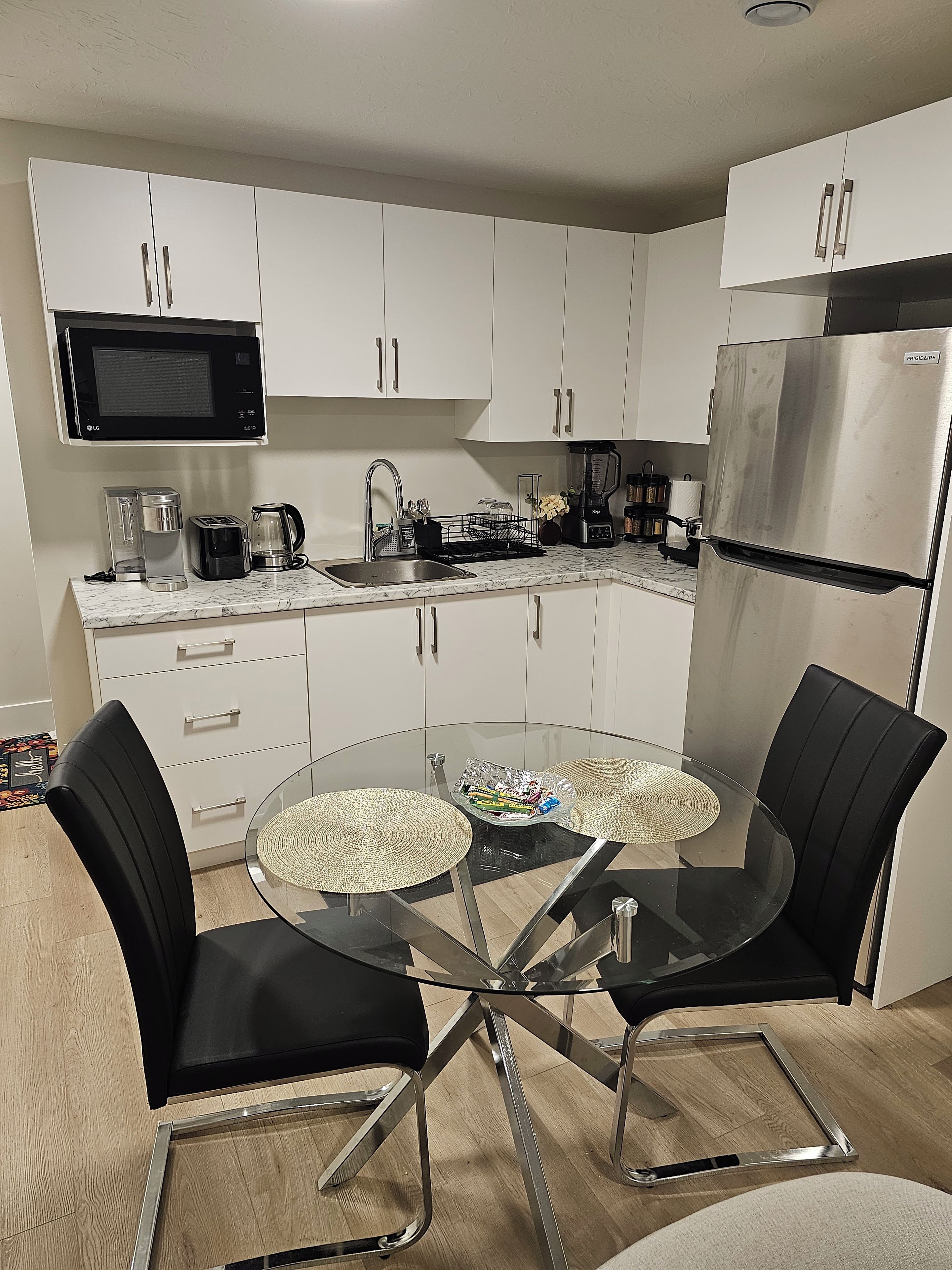A modern kitchen with white cabinets, a stainless steel refrigerator, a microwave, and a coffee maker.