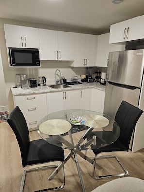 A modern kitchen with white cabinets, a stainless steel refrigerator, a microwave, and a coffee maker. - Chester Luxury Suites - Brand New Moncton Getaway (Moncton)