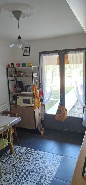 A kitchen with a microwave, shelves with various items, a hanging bag, and a window with curtains. - At the foot of the Alpilles, in the Arles-Avignon-Nîmes triangle (Saint-Étienne-du-Grès)