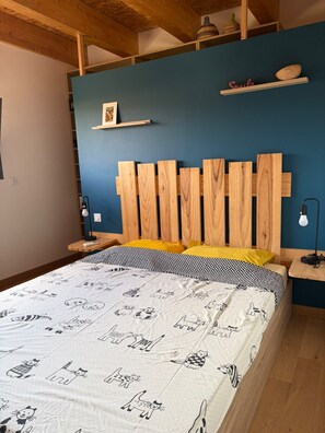 A bedroom with a wooden headboard, a bed with a patterned bedspread, a nightstand with a lamp, and a shelf with decorative items. - At the foot of the Alpilles, in the Arles-Avignon-Nîmes triangle (Saint-Étienne-du-Grès)
