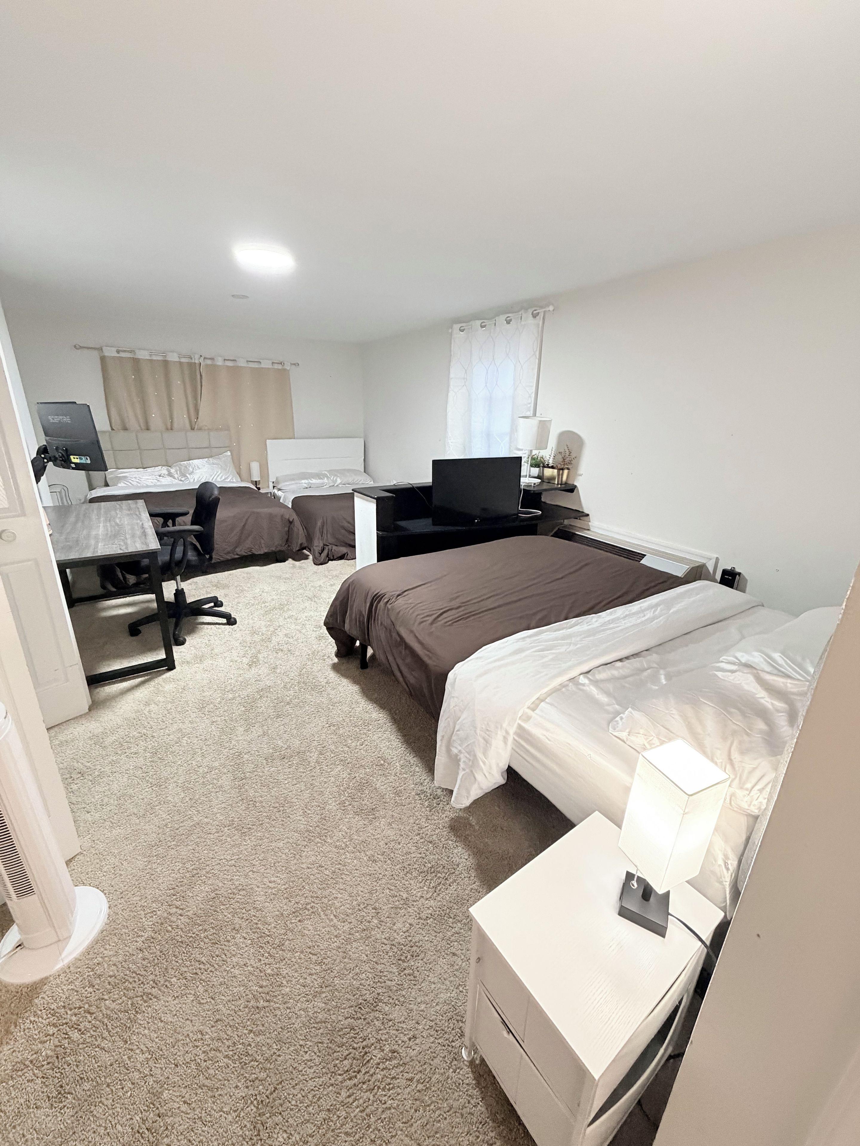 Una camera d'albergo con un letto, una scrivania con un computer, una sedia, una televisione e un comodino con una lampada.