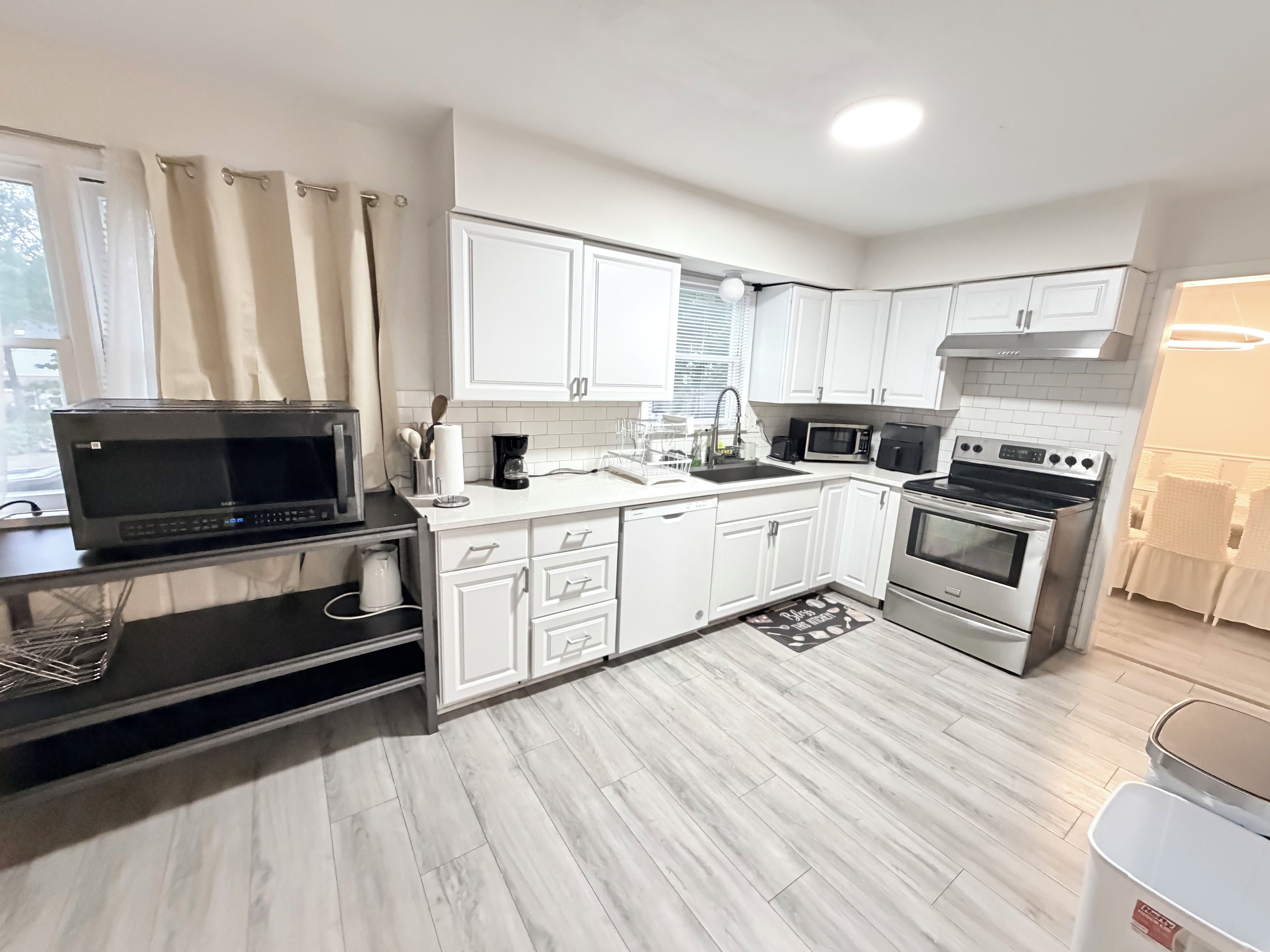 Een moderne keuken met witte kastjes, roestvrijstalen apparatuur en een zwart aanrechtblad met een magnetron.