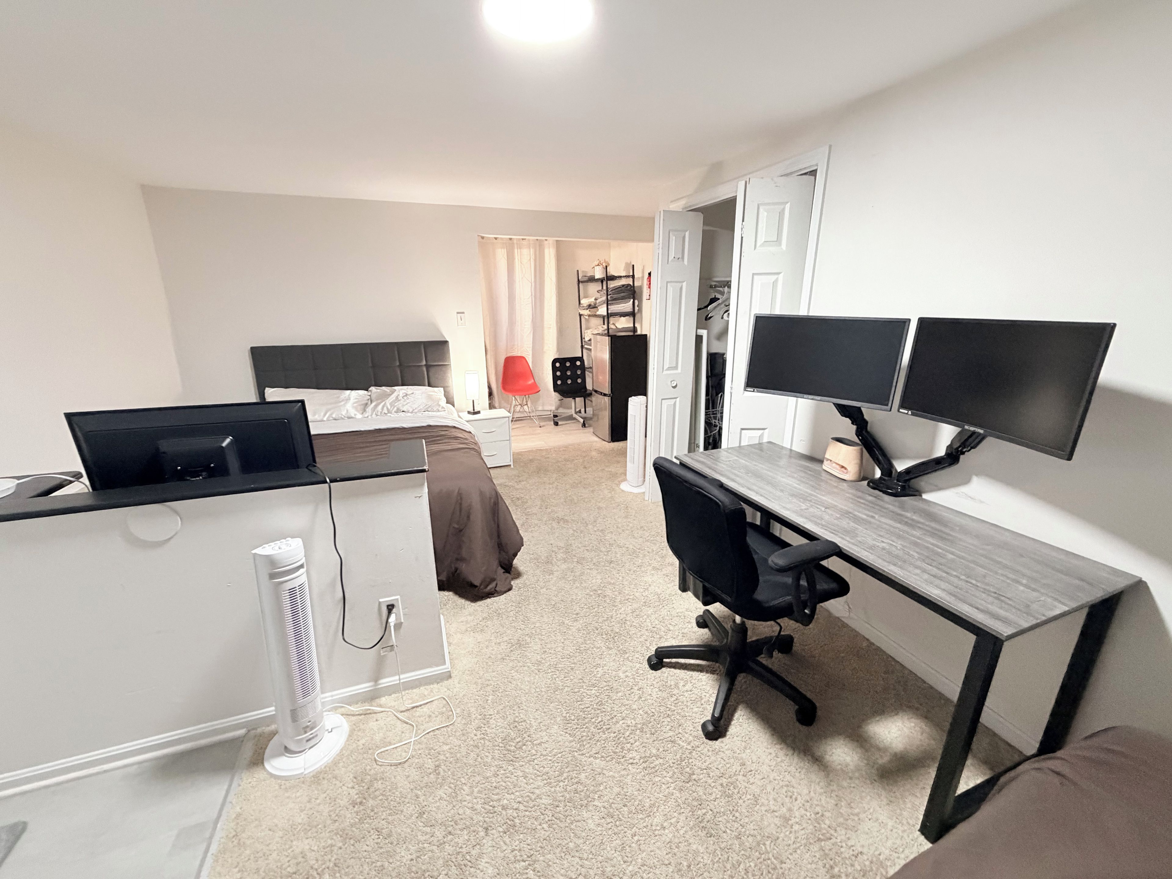 Une chambre à coucher avec un lit, un bureau doté de deux écrans, une chaise et un radiateur.