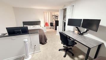 Ein Schlafzimmer mit einem Bett, einem Schreibtisch mit zwei Bildschirmen, einem Stuhl und einer Heizung.