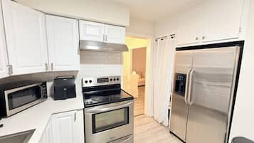 Eine moderne Küche mit weißen Schränken, einem Edelstahlkühlschrank, einem eingebauten Backofen und einer Mikrowelle.